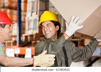 Happy Foreman With Coworker Lifting Cardboard Box At Warehouse