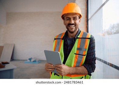 Happy foreman using digital tablet at renovating home and looking at camera.