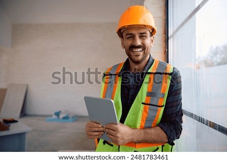 Happy foreman using digital tablet at renovating home and looking at camera.