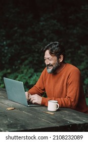 Happy Free Adult Man Work Outdoors On A Table With Nature In Background - Concept Of Digital Nomad Modern Online Lifestyle People - Mature Male With Beard Use Laptop Computer In The Woods Smiling 