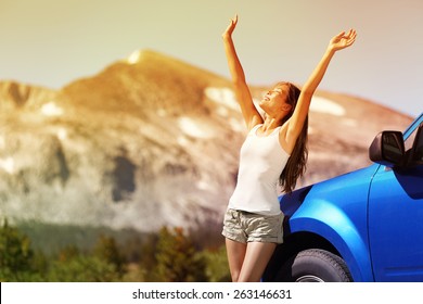 Happy Free Woman Next To Car Relaxing On Summer Road Trip Adventure Travel With Open Arms Up Showing Freedom. Nature Travel Concept With Mountain Background In The USA. Young Asian Adult Driver.