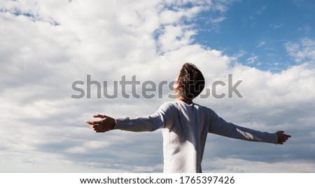 Happy and free young male person with open arms towards the blue sky. Feeling good and freedom.