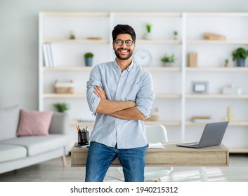 Happy Freelance Arab Guy Standing At Desk At Home Office, Posing And Smiling To Camera