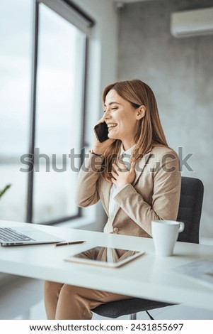 Happy freelancer using computer and talking on smart phone at office. Beautiful businesswoman working sitting at her desk in the office. Portrait of a happy executive wearing suit calling customer 
