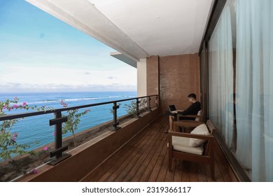 Happy freelancer using laptop and smartphone on balcony of villa with ocean view, millennial worker concept - Powered by Shutterstock