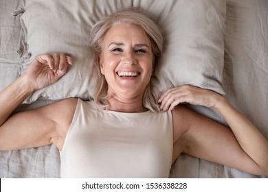 Happy Fresh Beautiful Mature Older Woman Awake After Healthy Sleep Stretch Wake Up In Cozy Comfortable Bed, Smiling Middle Aged Lady Enjoy Good Morning Looking At Camera, Close Up Portrait, Top View