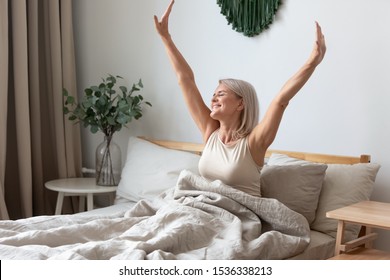 Happy fresh mature middle aged woman stretching in bed waking up alone happy concept, smiling old senior lady awake after healthy sleep sitting in cozy comfortable bedroom interior enjoy good morning - Shutterstock ID 1536338213