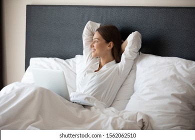 Happy Fresh Relaxed Young Woman Resting Sitting In Bed Wear Pajamas Using Laptop Enjoying Good Morning After Wakeup At Modern Home Hotel Bedroom Looking Outside Relaxing Alone With Device Concept