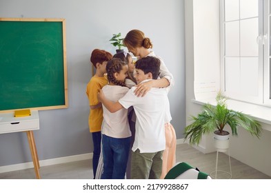 Happy Friendly Children Together Hug Teacher Woman After End Of Lessons, Not Wanting To Leave After End Of Training Stand In Classroom For Elementary School Students. Kids Education, Tutoring