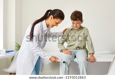 Happy, friendly doctor examining a child. Professional neurologist uses a hammer to test the knee jerk patellar reflex of a little school boy. Children, health, neurology, medical checkup concept