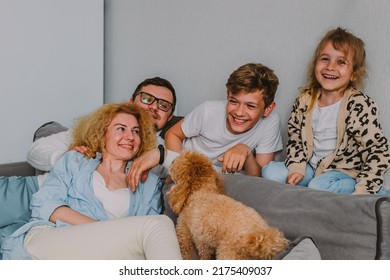  Happy Friendly Family Sits At Home On The Couch, Having Fun, Laughing. Parents Play With Their Children And Pets. Dad, Teenage Son, Little Daughter, Mom, A Red Poodle. High Quality Photo.