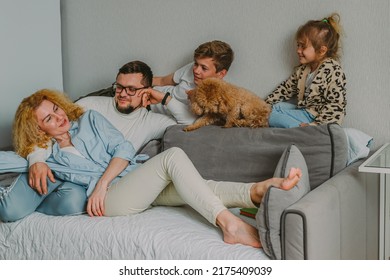  Happy Friendly Family Sits At Home On The Couch, Having Fun, Laughing. Parents Play With Their Children And Pets. Dad, Teenage Son, Little Daughter, Mom, A Red Poodle. High Quality Photo.