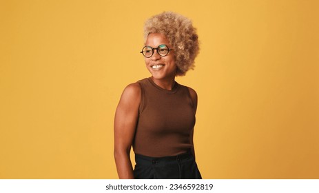 Happy friendly girl in glasses, wearing brown top smiling broadly laughing out loud with white teeth, isolated on orange background, studio shot - Shutterstock ID 2346592819