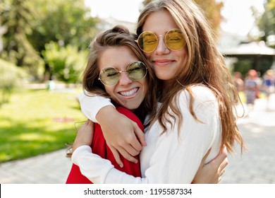 Happy friendly girls hugging each other with true smiles and having fun outside. Portrait  of two excited ladies expressing positive emotions enjoying walking. 
