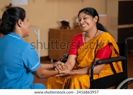 happy friendly Indian nurse or caretaker talking with recovered woman or patient on wheelchair - concept of professional occupation, compassion and encouragement