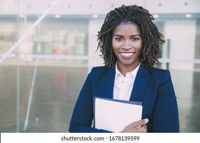 Happy Friendly Legal Expert Posing Outside. Young Black Business Woman Standing At Glass Wall, Holding Documents, Looking At Camera, Smiling. Legal Expert Concept