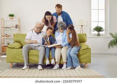 Happy friendly multigenerational family keep good memories of days gone by. Big multi generational family gather on the sofa in the living room interior and look through their photo album all together - Powered by Shutterstock