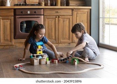 Happy Friendly Small Boy Girl Siblings Kids Sitting On Heated Warm Wooden Floor, Playing With Toy Railway Road In Kitchen, Enjoying Stress Free Leisure Weekend Time Together At Home, Playtime Activity