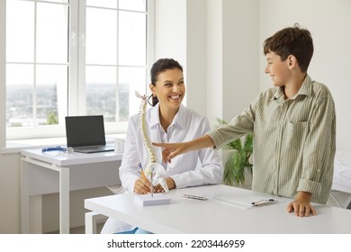 Happy, Friendly, Smiling Doctor At Orthopedic Clinic Communicating With Child, Showing Anatomical Spine Model, Telling About Skeleton And Spinal Curvatures And Explaining How To Prevent Back Problems