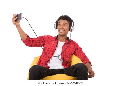 Happy friendly teenage boy with headphones taking selfie and listening to music, teenager wearing red shirt,  isolated on white background