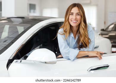 Happy friendly woman customer female buyer client wears blue shirt stand inside car chooses auto wants to buy new automobile in showroom vehicle salon dealership store motor show indoor. Sales concept