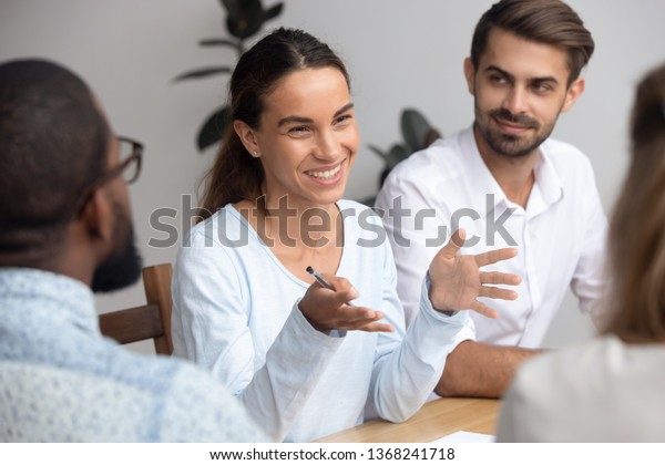 Happy friendly woman team leader coach\
mentor talking to employees group at office meeting smiling\
offering idea teaching interns or reporting at briefing seminar\
having fun business\
conversation