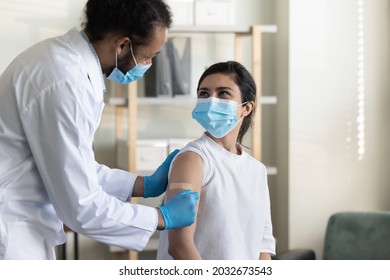 Happy Friendly Young African American Physician Family Doctor In Medical Uniform Gluing Patch On Hand Of Smiling Indian Ethnicity Woman After Injection, Finishing Anti Covid Vaccination In Clinic.