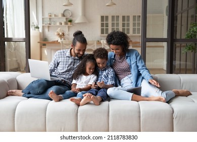 Happy friendly young African American couple parents and small adorable kids son daughter using different gadgets, playing games, web surfing, spending time online or shopping, modern tech addiction. - Powered by Shutterstock