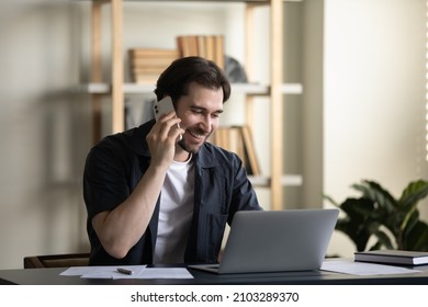 Happy friendly young businessman manager employee involved in phone call conversation, consulting client or discussing project with partner, multitasking working on computer in modern home office, - Powered by Shutterstock