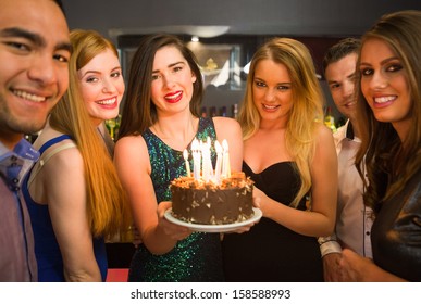 Happy friends celebrating brithday one holding birthday cake looking at camera in a nightclub