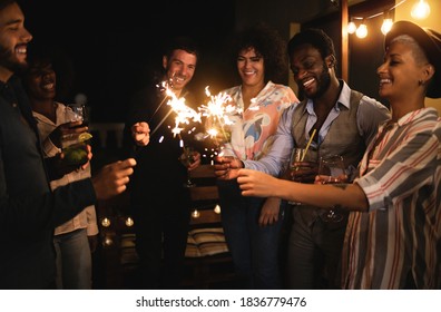 Happy friends celebrating with fireworks at new year's eve party - Soft focus on african man face - Powered by Shutterstock