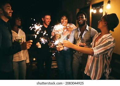 Happy friends celebrating with fireworks at new year's eve party - Soft focus on african man face