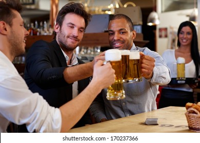 Happy friends clinking with beer mugs in pub, smiling. - Powered by Shutterstock