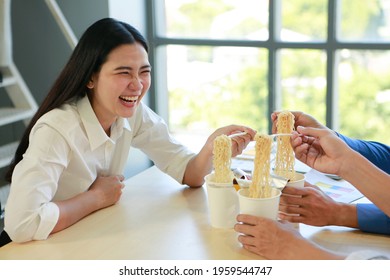 Happy Friends Or Colleagues Sitting Together And Eating Noodles With Chopsticks On Table At Home Office Near Window And Stair With Copy Space And Garden Background. Lunch Enjoy Asian Fast Food Concept