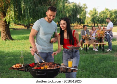 Happy friends cooking meat and vegetables on barbecue grill in park