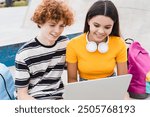 Happy friends couple of college students school pupils teenagers boy girl classmates holding using laptop doing homework study remote watching video play games sitting in skate park ramp after lessons