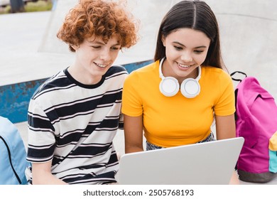 Happy friends couple of college students school pupils teenagers boy girl classmates holding using laptop doing homework study remote watching video play games sitting in skate park ramp after lessons - Powered by Shutterstock