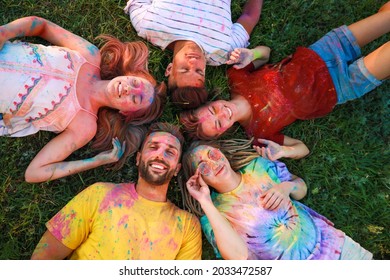 Happy friends covered with colorful powder dyes on green grass outdoors, above view. Holi festival celebration