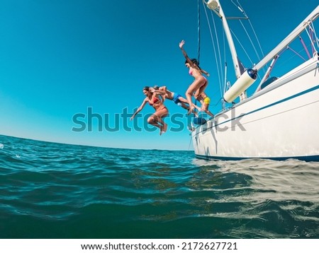 Happy friends diving from sailing boat into the sea - Soft focus on left girl face