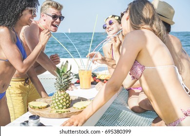 Happy friends drinking tropical cocktails and eating pineapple fruit at boat party - Young people having fun on summer vacation - Youth, travel and holidays concept - Main focus on blond man 