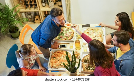 Happy friends eating pizza and drinking beers at home - Young people having fun at dinner together - Friendship concept - Focus on hand holding pizza slice