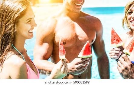 Happy Friends Eating Watermelon In Swimming Pool Resort Hotel - Young Handsome People Having Fun Tasting Tropical Fresh Fruits - Summer Vacation Concept - Focus On Left Girl Eye - Warm Contrast Filter