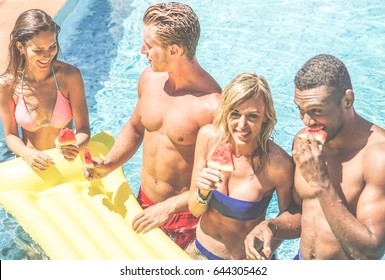 Happy Friends Eating Watermelon In Swimming Pool Hotel Resort -  Diverse Culture Couples Having Fun In Summer Vacation - Travel, Youth, Holidays Concept - Focus On Left Girl - Warm Cinematic Filter 