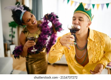 Happy Friends Enjoying In Drinks While Celebrating Mardi Gras At Home Party. Focus Is On Man Drinking Cocktail.