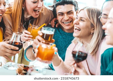 Happy friends enjoying happy hour sitting at bar restaurant table - Young people having fun hanging out on weekend day - Food and beverage concept with guys and girls drinking alcohol together 