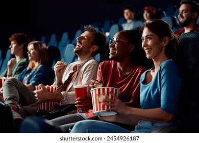 Happy friends enjoying in movie projection in theater. Focus is on African American woman eating popcorn.  - Powered by Shutterstock