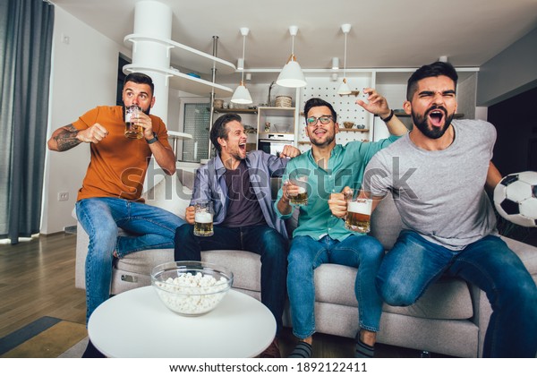 Happy friends and football fans watching\
football on tv and celebrating victory at\
home
