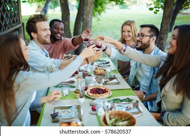 Happy friends with glasses of red wine toasting by festive table - Powered by Shutterstock