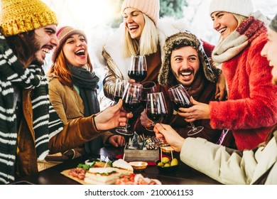 Happy Friends Group Toasting Red Wine Dining At Restaurant Terrace - Young People Socializing Drinking And Eating Food Sitting Outside At Winery Bar Table - Winter Season - Dinner Lifestyle Concept