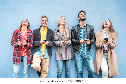 Happy friends group using smartphones against blue wall at university college break - Young people having fun with mobile smart phone - Technology addiction concept with always connected millennials